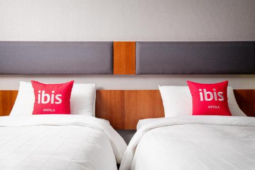 two beds with red pillows in a hotel room at Ibis Ambassador Myeongdong in Seoul