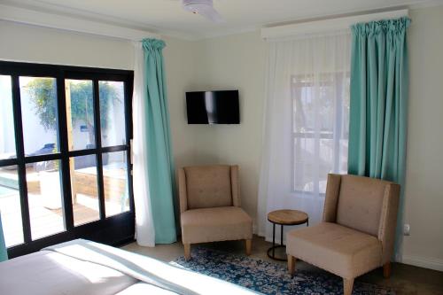a bedroom with a bed and two chairs and a television at Whale Rock Luxury Lodge in Hermanus