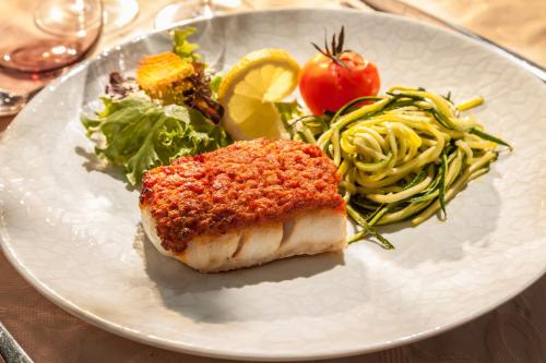 a white plate with a piece of fish and salad at Le Domaine de Falgos Golf & Spa in Saint-Laurent-de-Cerdans