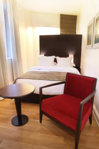 a bedroom with a bed and a red chair and a table at Logis Hôtel Ettenheim in Strasbourg