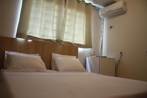 1 cama con almohadas blancas en una habitación con ventana en Hotel Friburgo, en Cidade Ocidental