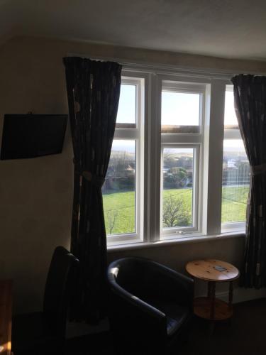a room with two windows with a chair and a table at Woodthorpe Hotel in Skegness