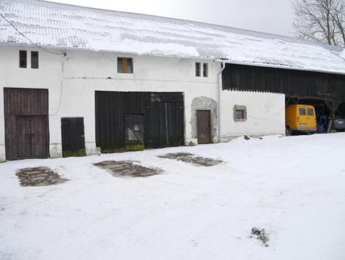 a white building with a barn with snow on the ground at Pod kasztanem gospodarstwo agroturystyczne in Stronie Śląskie