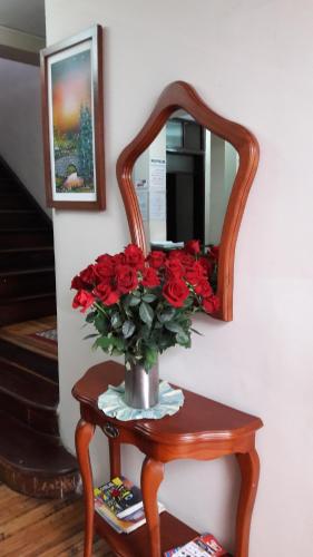 a vase of red roses on a table with a mirror at Hostal Santa María Gracia in Quito