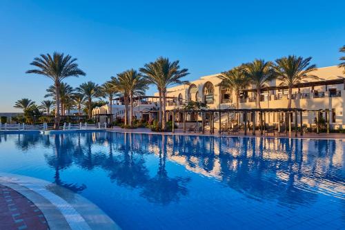une grande piscine avec des palmiers et des bâtiments dans l'établissement Jaz Belvedere Resort, à Charm el-Cheikh
