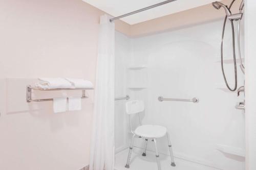 baño blanco con ducha y taburete en Travelodge by Wyndham Chattanooga/Hamilton Place, en Chattanooga