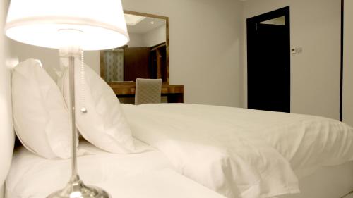 a bed with white sheets and a lamp on it at Broad Almkan Apart Hotel in Taif