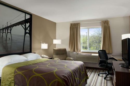 a hotel room with a bed and a desk and a window at Super 8 by Wyndham Manistee in Manistee
