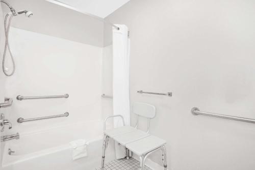 a white bathroom with a chair and a bath tub at Super 8 by Wyndham Canandaigua in Canandaigua
