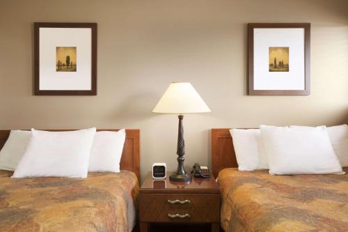 a hotel room with two beds and a lamp on a table at Central Suite Hotel in Lloydminster