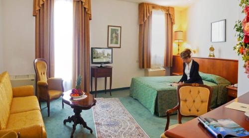 a man sitting in a hotel room next to a bed at Hotel In Sylvis in Sesto al Reghena