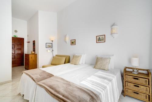 a white bedroom with a large bed and a chair at Sunrise Apartment I in Carvoeiro