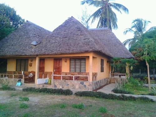 a house with a thatched roof and a palm tree at Mango Lodge MSAMBWENI in Kisimachande