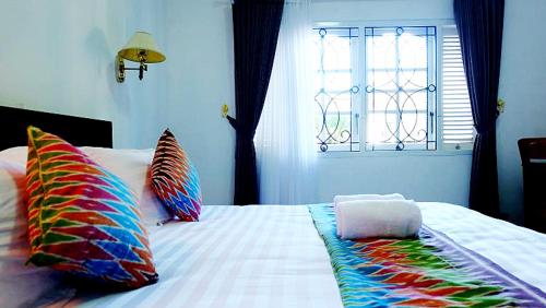 a bed with colorful pillows on it with a window at City Stay Homestay Jogja in Yogyakarta