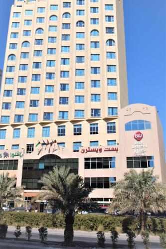 a large white building with palm trees in front of it at Best Western Plus Mahboula in Kuwait