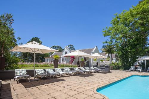 a patio with chairs and umbrellas next to a pool at Lairds Lodge Country Estate in Plettenberg Bay