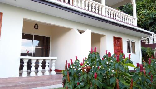 a white house with a red door and a plant with red flowers at Precious Residence C in Grand'Anse