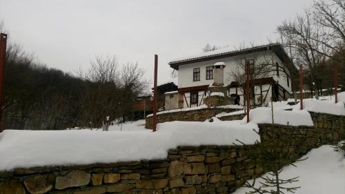 a house with a stone wall in the snow at Къща за гости Ножери in Tryavna