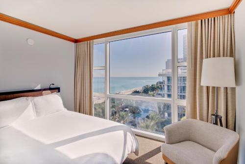 1 dormitorio con cama, silla y ventana grande en Carillon Miami Wellness Resort, en Miami Beach