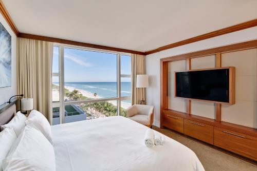 a hotel room with a bed, television and a balcony at Carillon Miami Wellness Resort in Miami Beach
