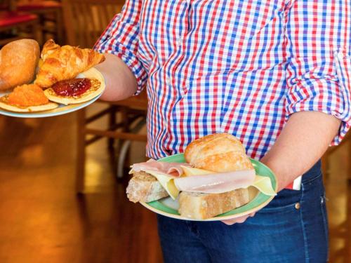 a person holding a sandwich and pastries on a plate at Hotel ibis Lisboa Jose Malhoa in Lisbon