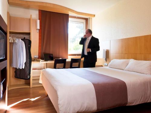 ブリュッセルにあるイビス ホテル ブリュッセル エクスポ アトミウムのベッド付きのホテルルームに立つ男