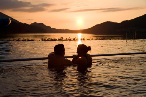 a man and woman sitting in the water at sunset at Haus Bergblick in Fuschl am See