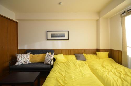 a bedroom with a bed with yellow sheets and a couch at Apartment Zen Hotel in Mizuho
