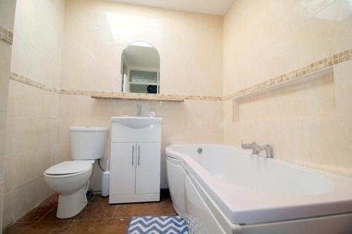 a bathroom with a toilet and a tub and a sink at Pebbles Beach House By Air Premier in Seaford