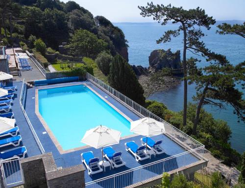 uma piscina com cadeiras e guarda-sóis junto ao oceano em The Imperial Torquay em Torquay