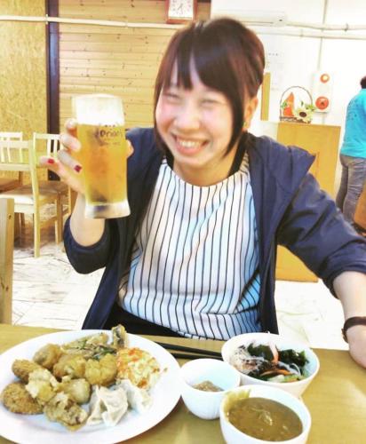 a woman holding a glass of beer next to a plate of food at 宮古島サイクリストの宿 in Miyako Island