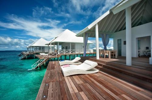 a wooden deck with two white chairs on the water at Diamonds Thudufushi Maldives Resort & Spa in Thundufushi