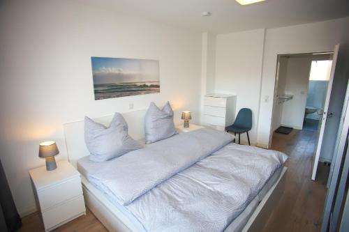 a white bedroom with a bed with white sheets and pillows at Appartementanlage Wieben in Sankt Peter-Ording