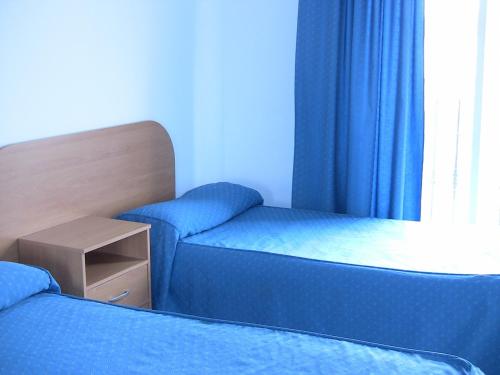 two beds in a room with blue curtains at Apartahotel Los Hermanos in Ocaña