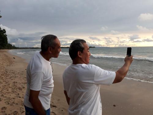 two men standing on the beach taking a picture at Lippo Carita Beach Utara Condo Noah in Carita