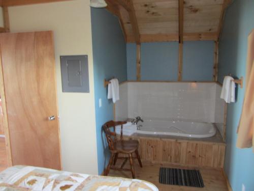 a bathroom with a tub and a chair and a bed at Chalets Nature Océan in Perce