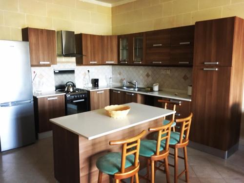 uma cozinha com armários de madeira e uma ilha de cozinha com bancos de bar em Masri Accommodation em Il-Pergla