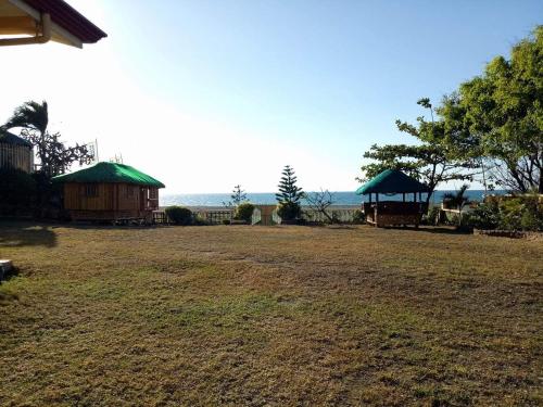 a field with two huts and a house and the ocean at Seabreeze Beachfront Home and Cottages new management in San Juan