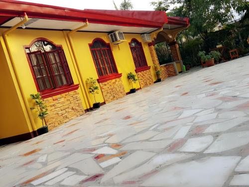 a yellow house with red windows and a driveway at Carribean Transient House in Lucap