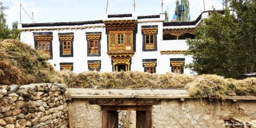 a white building with windows and a wall with hay at Nimmu House Ladakh in Nimu