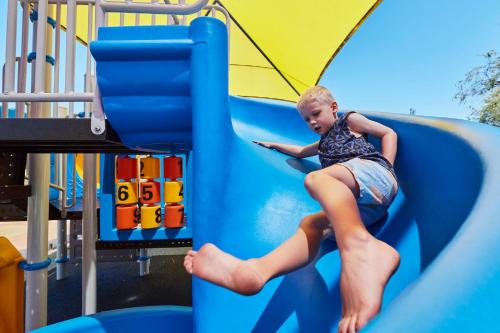 a young girl is sliding down a slide at a playground at BIG4 Breeze Holiday Parks - Busselton in Busselton
