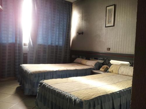 two beds in a hotel room with the sun shining at Hotel La Giralda in Nador