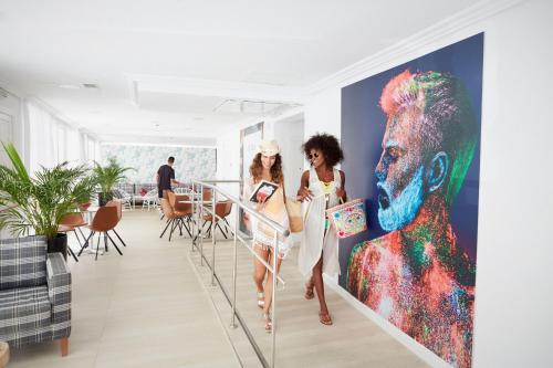 two women walking in a room with a painting of a man at Hotel Vibra Lei Ibiza - Adults only in Ibiza Town