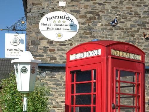 uma cabine telefónica vermelha em frente a um edifício de tijolos com uma placa em Henblas Hotel em Altenaffeln