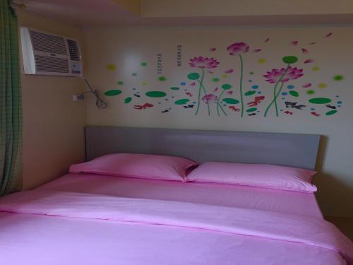 a bedroom with a bed with pink sheets and flowers on the wall at Avida Towers Condotel in Davao City