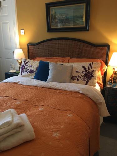 a bed with an orange comforter and pillows at Wynberg House Bed & Breakfast Swansea in Swansea