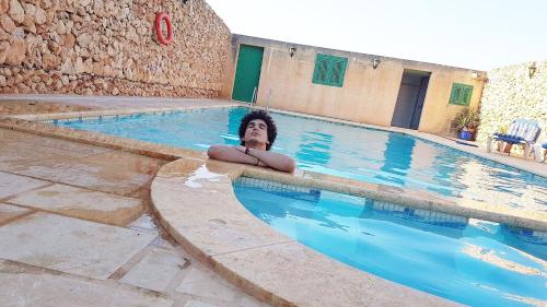 Um homem está deitado numa piscina. em Masri Accommodation em Il-Pergla