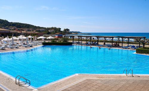 a large swimming pool with chairs and the ocean at Aldemar Olympian Village in Olympia