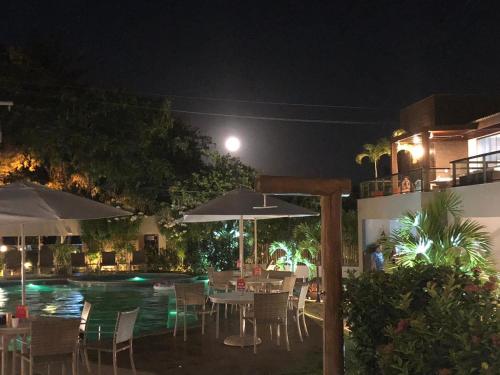una piscina con mesas y sombrillas por la noche en Imbassaí Solaris Village 2 quartos, en Imbassai