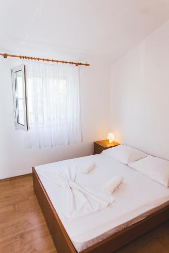 a bedroom with a bed with white sheets and a window at Apartmani Maleš in Rogoznica